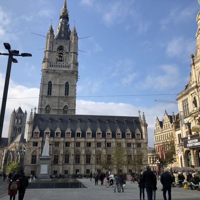 Blick auf ein typisch belgisches Gebäude, der Belfried. Zu einem fünfstöckigen Haus gehört ein hoher viereckiger Turm mit kleinen Türmen an jeder Ecke und spitzen Dächern.
