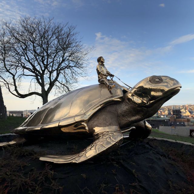 Auf einer großen Bronzeschildkröte sitzt ein kleiner Mann.