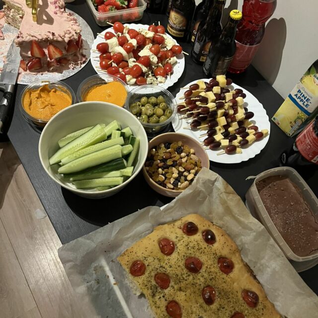 Bild von oben auf ein Buffet mit selbstgebackenem Focaccia, Gurken, Tomate-Mozzarella, Käse-Trauben-Spieße und Hummus.