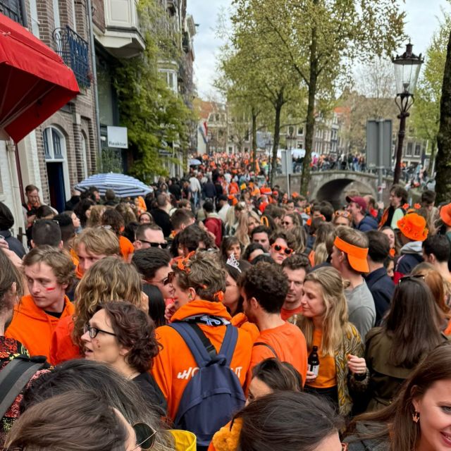 Blick auf viele Menschen, die orange Kleidung und Hüte tragen. Im Hintergrund stehen grüne Bäume.
