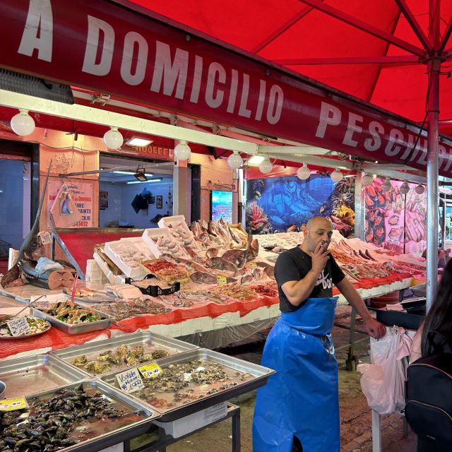 Ein Marktverkäufer steht vor seinem Stand und raucht. Auf dem Stand sieht man eine große Auswahl an Fisch und Meeresfrüchten.
