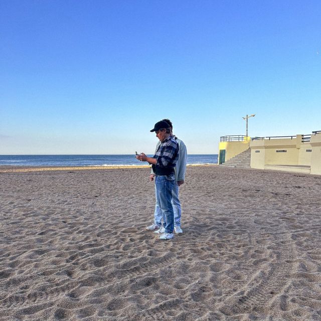 Zwei Männer stehen am Strand, rechts ist eine Promenade zu sehen