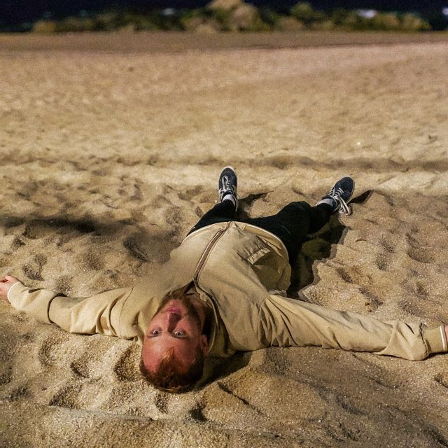 Junger Mann liegt am Strand kopfüber.