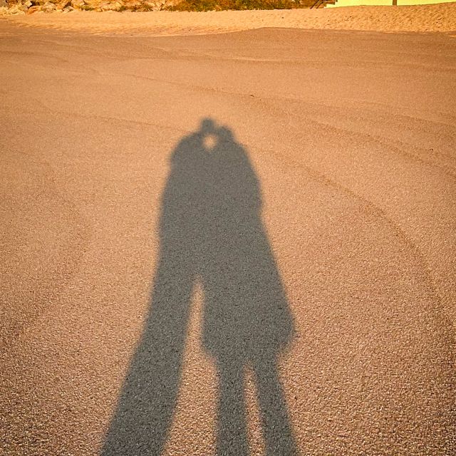 Der Schatten eines Pärchen, welches sich küsst auf dem Sandboden eines Strandes.